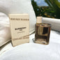 Burberry Her perfume bottle and packaging on a white surface with blurred greenery in the background