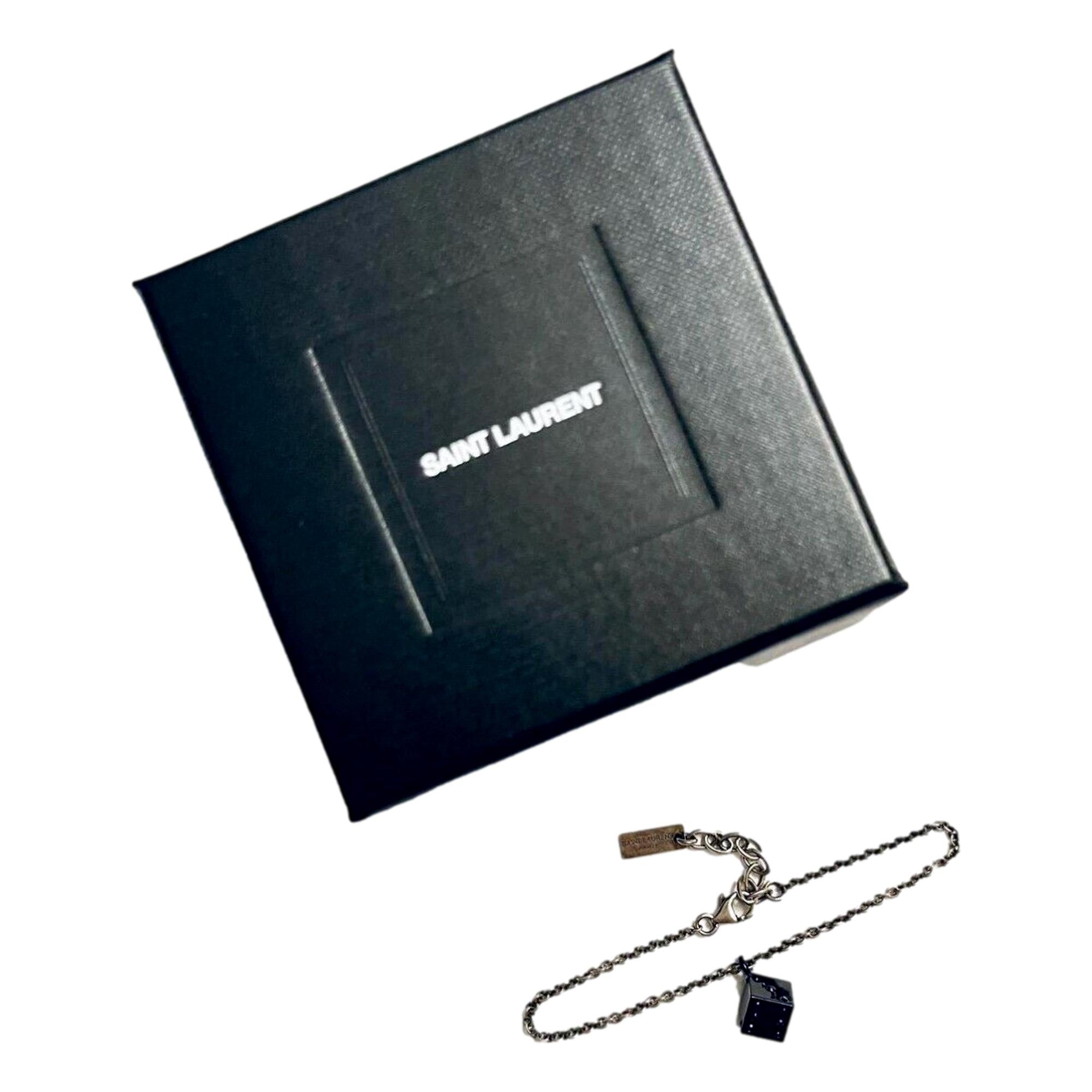 Sleek Saint Laurent Bracelet: Viscose Radio Black & Silver Charm -  The Saint Laurent Des Toile Viscose Radio Chain Bracelet offers a sleek, sophisticated touch to your look. Featuring a silver-tone design complemented by a black dice charm, this bracelet adds subtle boldness and a hint of fortune to your style. Model: 571859Silver-tone chainBlack dice charmLobster claw closureMetal tag with logo embossedIncludes authenticity cards and boxMade in Italy Shop Bags 