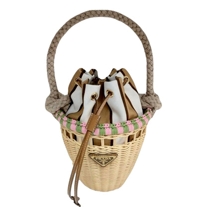 A Prada wicker bucket bag with a braided rope handle, featuring a white and brown leather bucket insert, a pink and green woven trim, and a gold-tone metal logo plaque on the front.