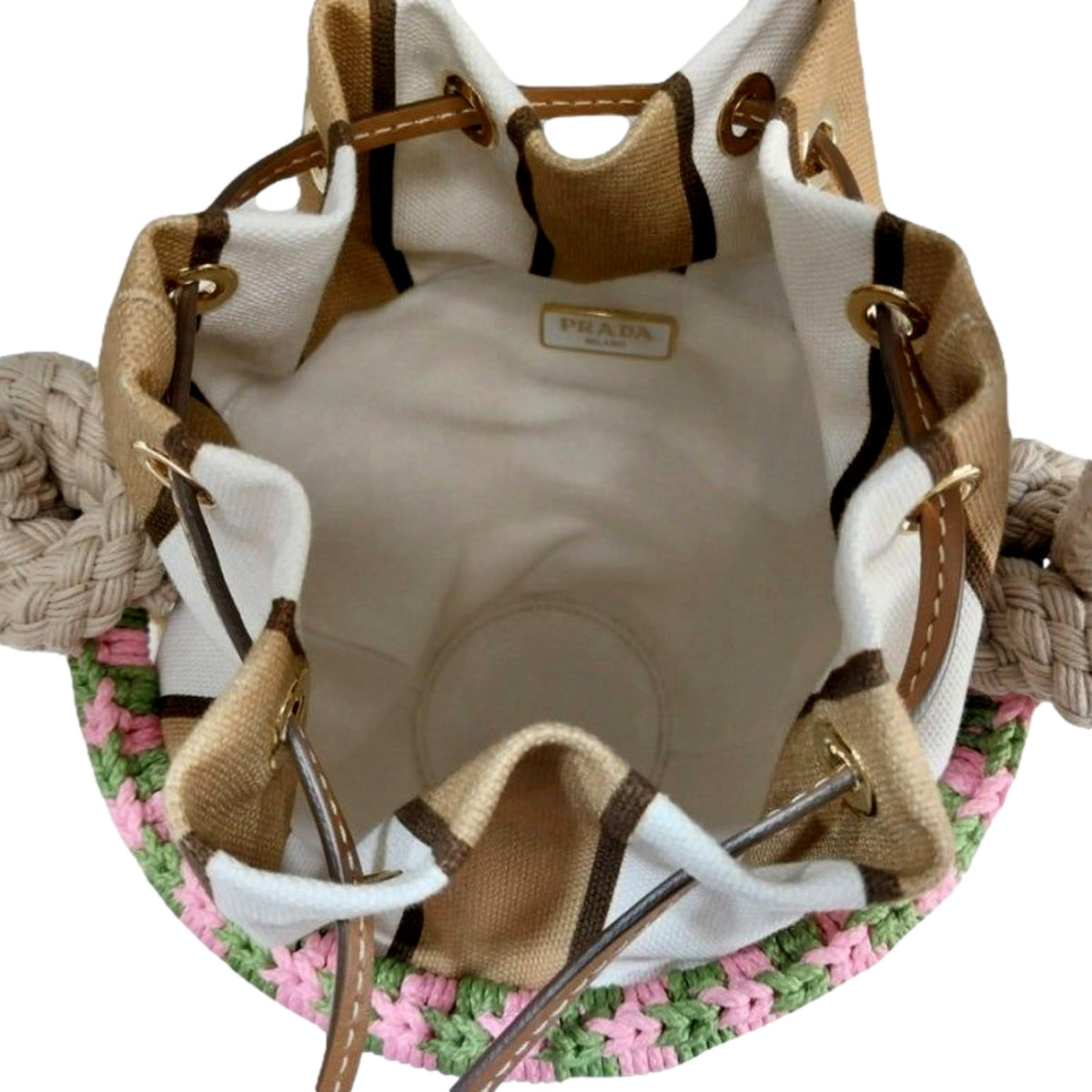 An open Prada bucket bag made of beige canvas and white fabric, with brown leather trim, gold-tone hardware, and a pink and green crocheted trim along the bottom. The interior lining is cream-colored, and a Prada logo label is visible inside.