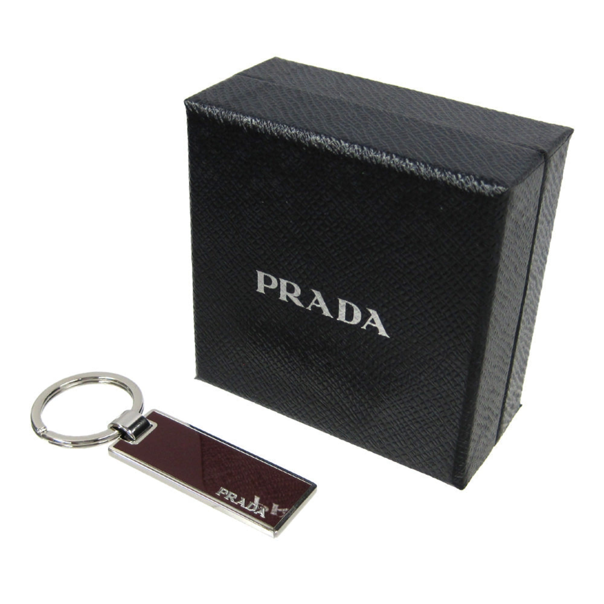Prada Rubino Red Enamel Keychain - Luxury Silver Metal Keyring -  This Prada Keychain features a sleek rectangular silver-tone base topped with deep burgundy red enamel. Designed for both men and women, it offers a sophisticated way to secure keys or accessorize a bag with a touch of luxury.Model number: 2PS021Rubino red enamelSilver-tone metal and key ring, 1.1" diameterMeasurements: 0.6 x 0.1 x 2" (LWH)Includes authenticity cards and Prada boxMade in Italy Shop Bags 